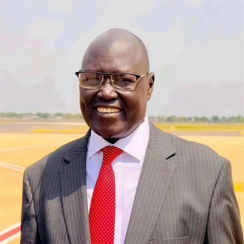 Prof. Kuel Maluil Jok, in a grey pinstripe suit and red tie, smiling outdoors